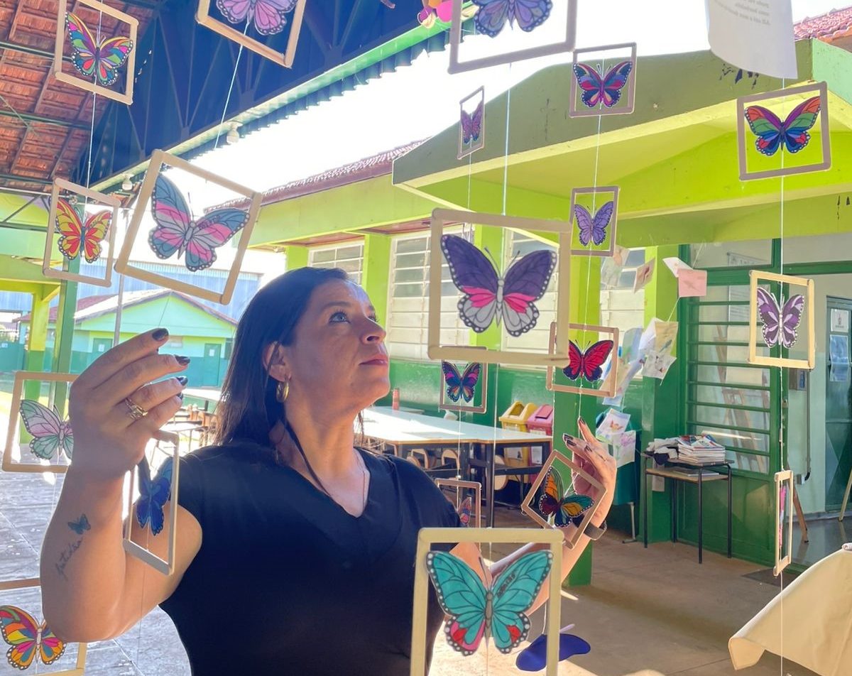 Mulher entre quadros com borboletas pendurados.