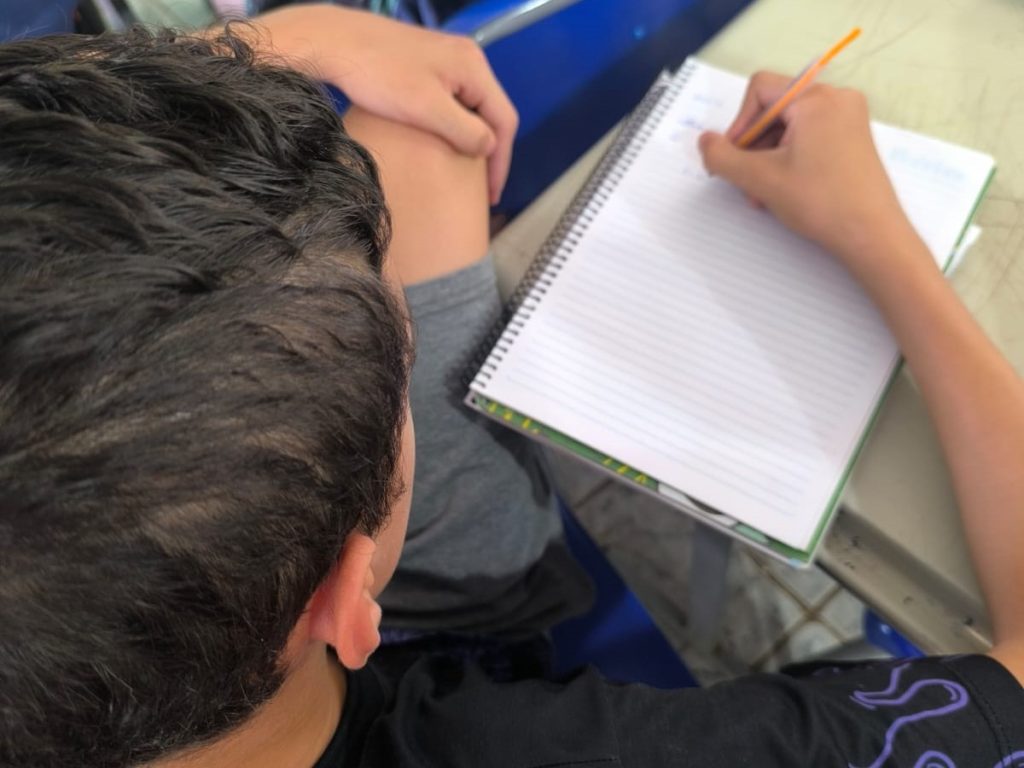 Estudante observando aula e anotando no caderno.