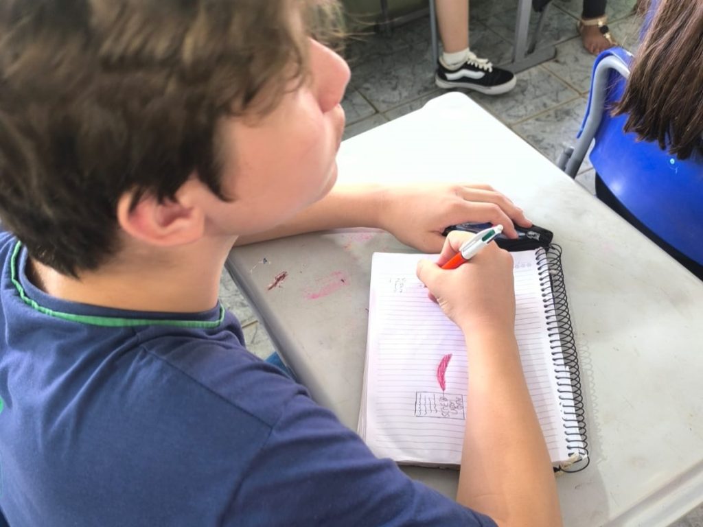 Estudante observando aula e anotando no caderno.