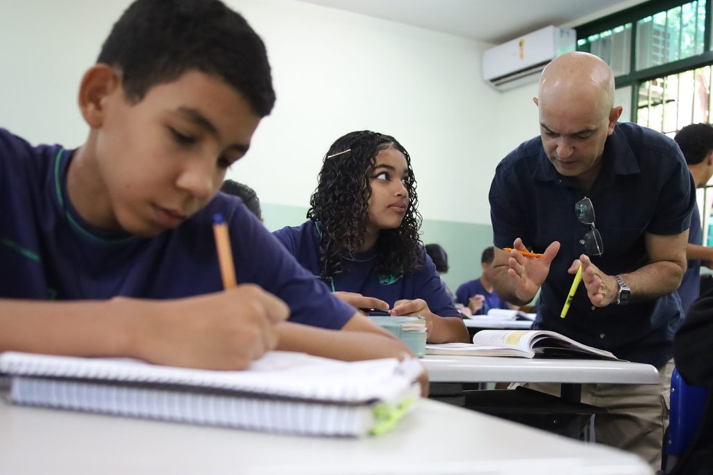 Estudante escrevendo na sala de aula com camiseta azul.
